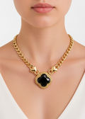 Gold chain necklace with a black clover pendant on a neutral background